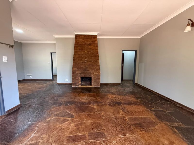 Spacious living room featuring a prominent brick fireplace and unique flagstone flooring, offering a neutral canvas for interior design.
