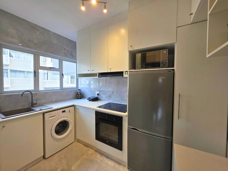 Modern kitchen featuring sleek white cabinetry, stone countertops, integrated appliances, and a tiled backsplash with a functional layout.