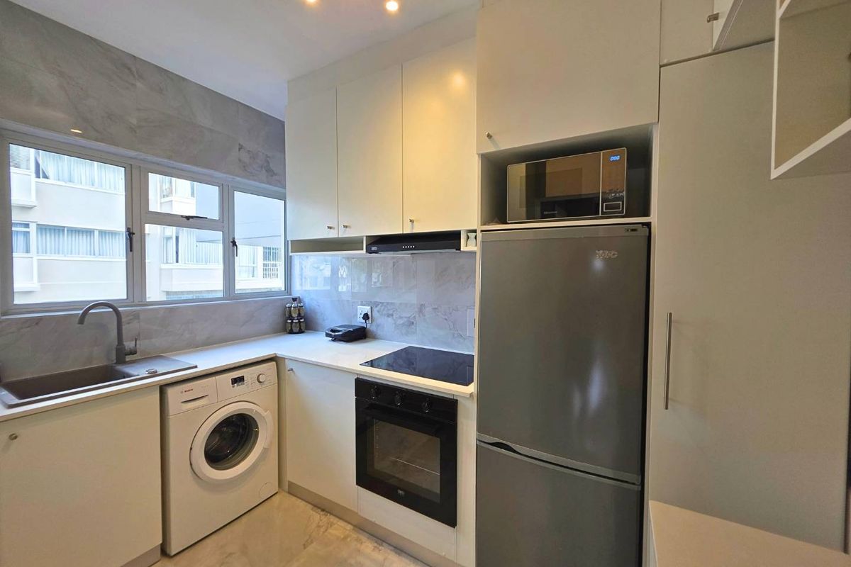 Modern kitchen featuring sleek white cabinetry, stone countertops, integrated appliances, and a tiled backsplash with a functional layout.