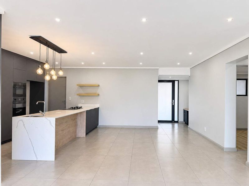 Modern open-plan kitchen and living area featuring a stone-topped island, built-in appliances, recessed lighting, and neutral tiled flooring throughout.