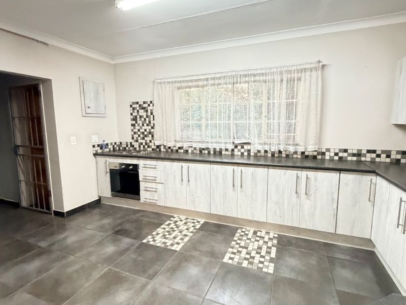 A spacious, empty kitchen featuring light-toned built-in cabinetry, a built-in oven, hob, and dark tiled flooring with decorative mosaic accents.