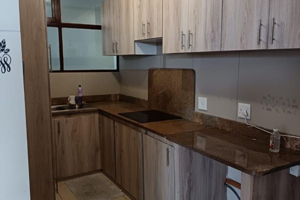 A functional kitchen featuring wood-look laminate cabinetry, granite countertops, an electric hob, and tiled flooring, with space for under-counter appliances.