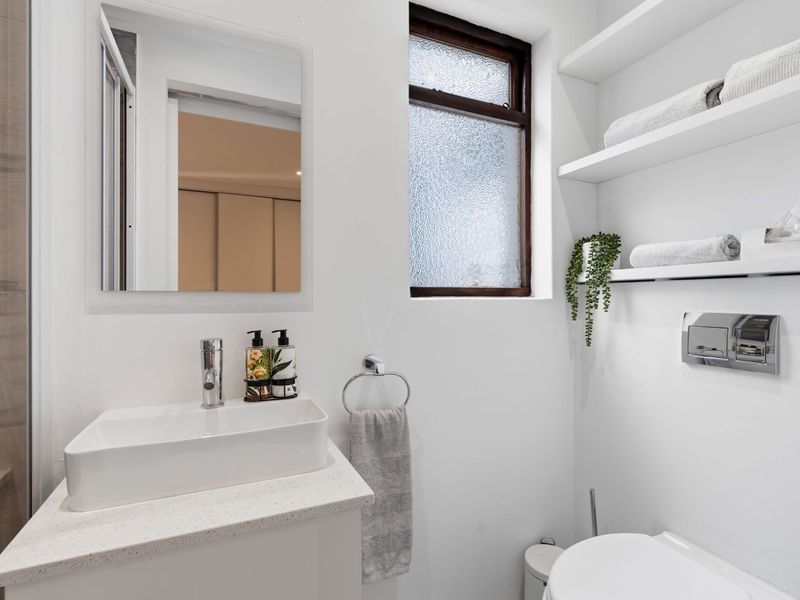 A modern, compact bathroom featuring a vessel sink on a stone vanity, wall-hung toilet with integrated flush plate, and convenient floating storage shelving.