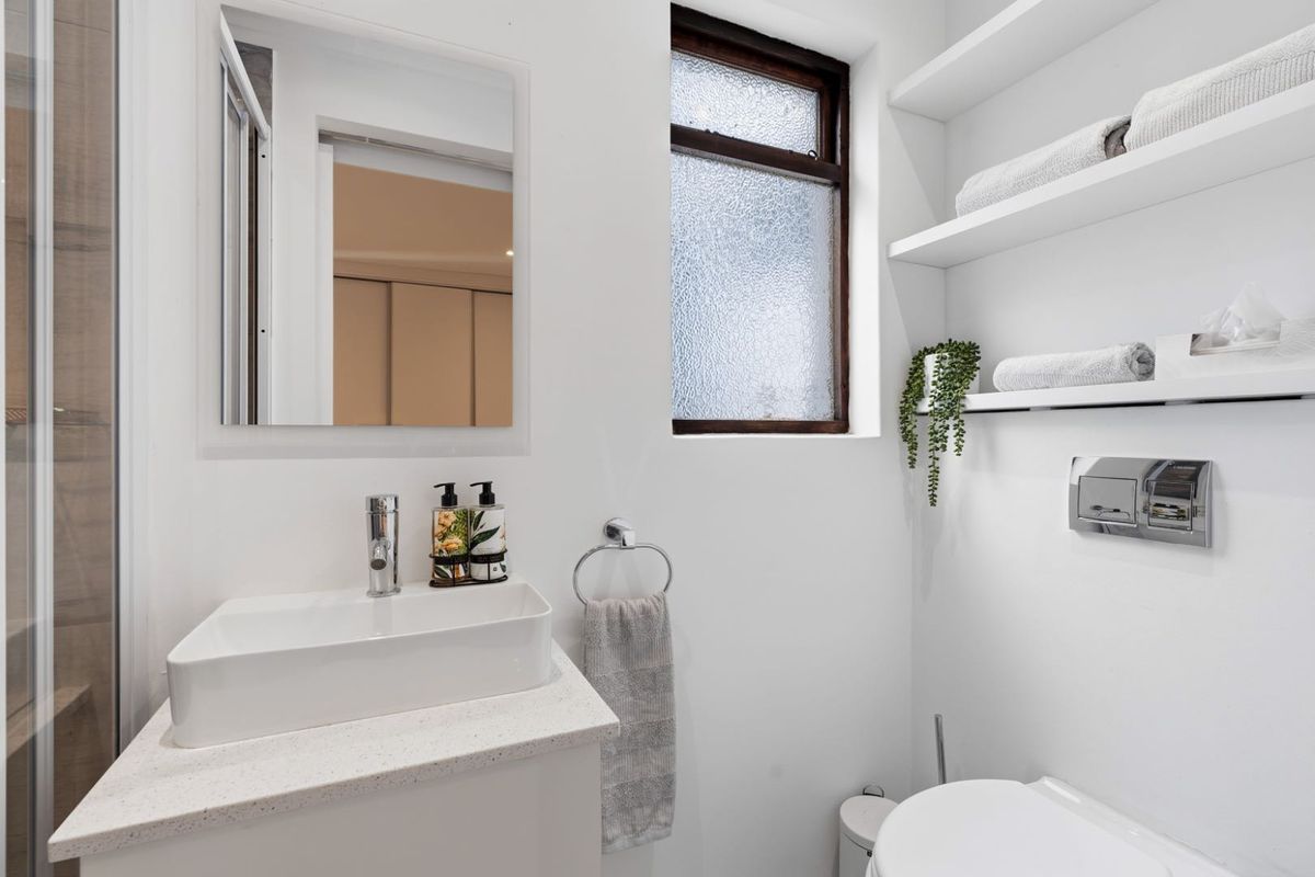 A modern, compact bathroom featuring a vessel sink on a stone vanity, wall-hung toilet with integrated flush plate, and convenient floating storage shelving.