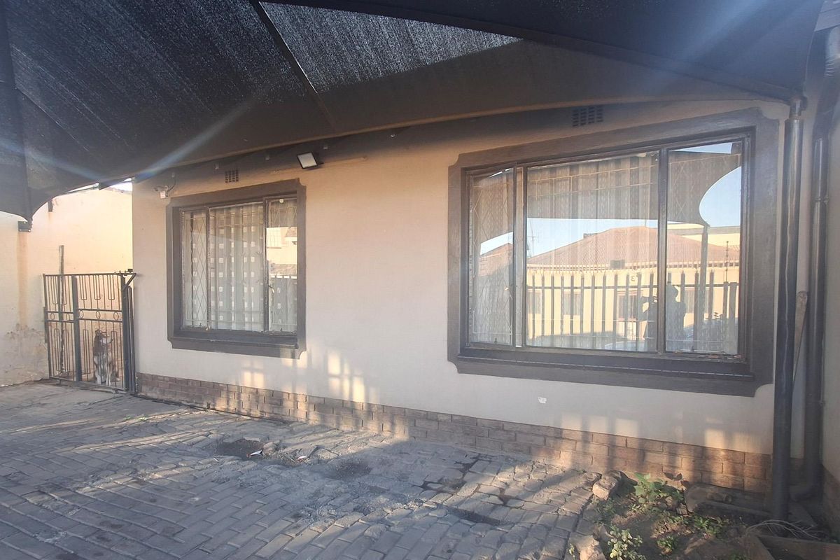 Rear exterior view of the property featuring a paved patio area covered by a shade sail and aluminium window frames.