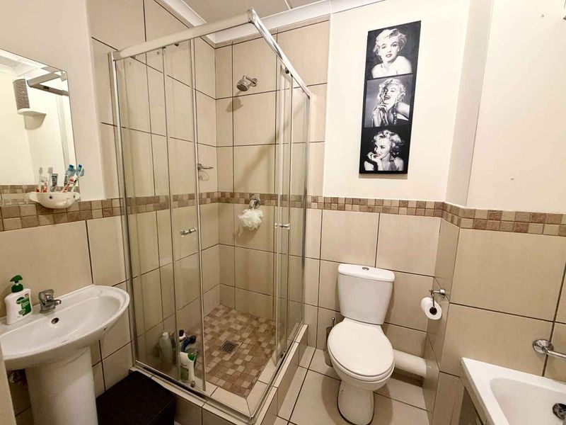 A functional bathroom featuring a glass shower enclosure, pedestal basin, and toilet with neutral wall and floor tiling.