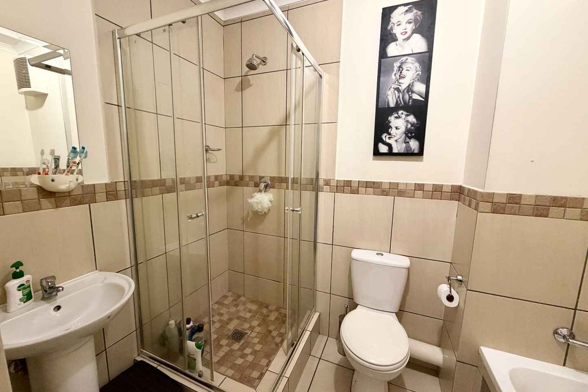 A functional bathroom featuring a glass shower enclosure, pedestal basin, and toilet with neutral wall and floor tiling.