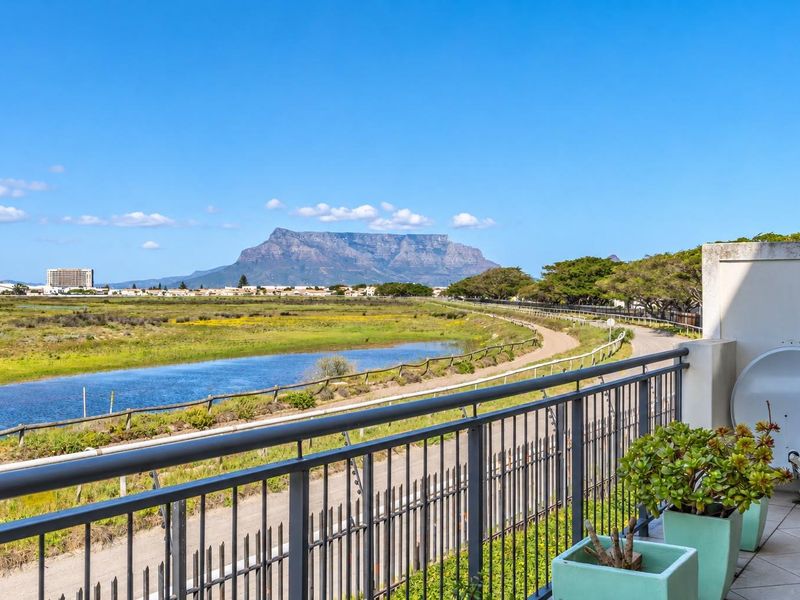 A spacious balcony featuring a metal balustrade and tiled flooring, offering expansive views of the surrounding landscape and Table Mountain.