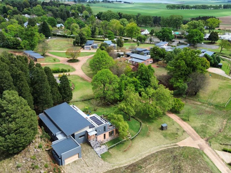 Aerial view of a modern residential property featuring a metal roof, solar panels, and a spacious landscaped garden within a scenic estate setting.