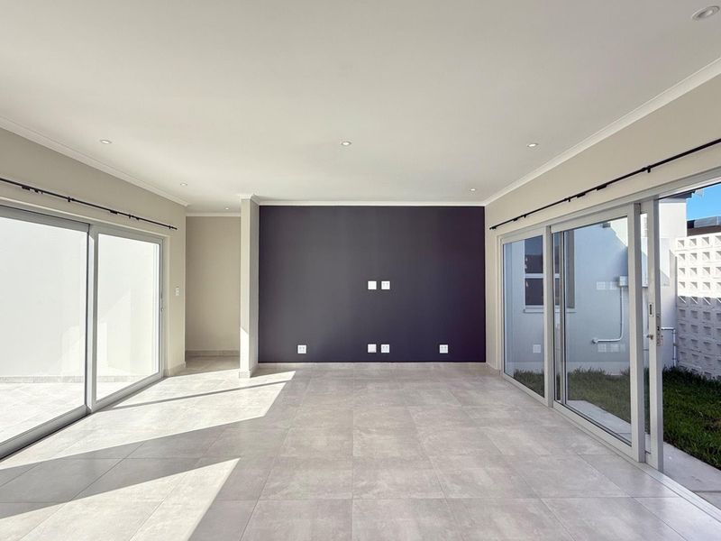 Spacious, light-filled living area featuring large sliding glass doors, neutral tiled flooring, and a modern dark accent wall.