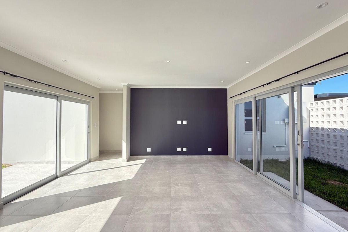 Spacious, light-filled living area featuring large sliding glass doors, neutral tiled flooring, and a modern dark accent wall.