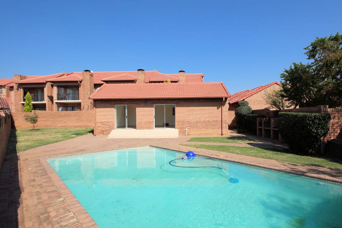 A rear view of the apartment featuring a private swimming pool, brick facade, tiled roof, and a paved patio area.