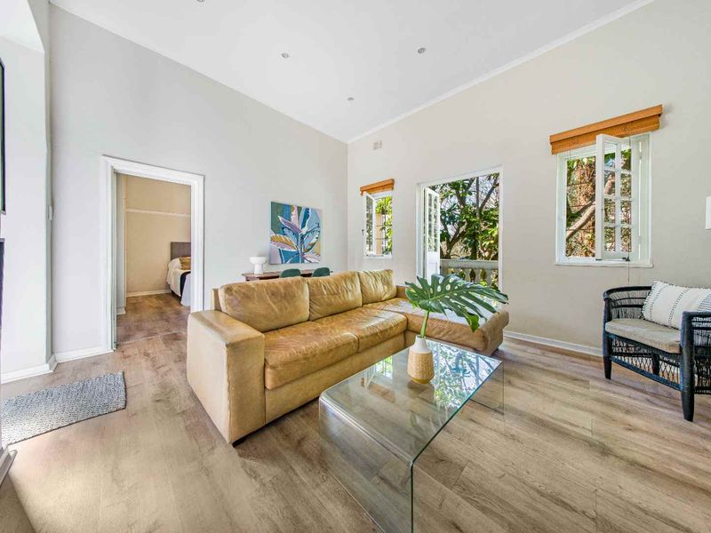 Bright and airy living room featuring light-toned laminate flooring, high ceilings, and large windows with access to an outdoor balcony area.