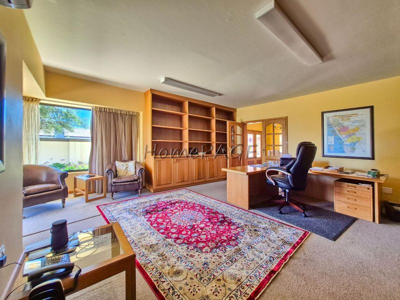 Spacious home office featuring extensive built-in wooden cabinetry, large windows, and classic french doors, providing a functional and well-lit workspace.