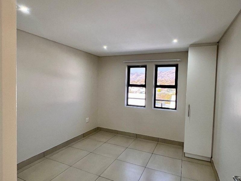 A clean, empty bedroom featuring neutral tiled flooring, recessed downlights, and a built-in cupboard, offering a bright and versatile living space.
