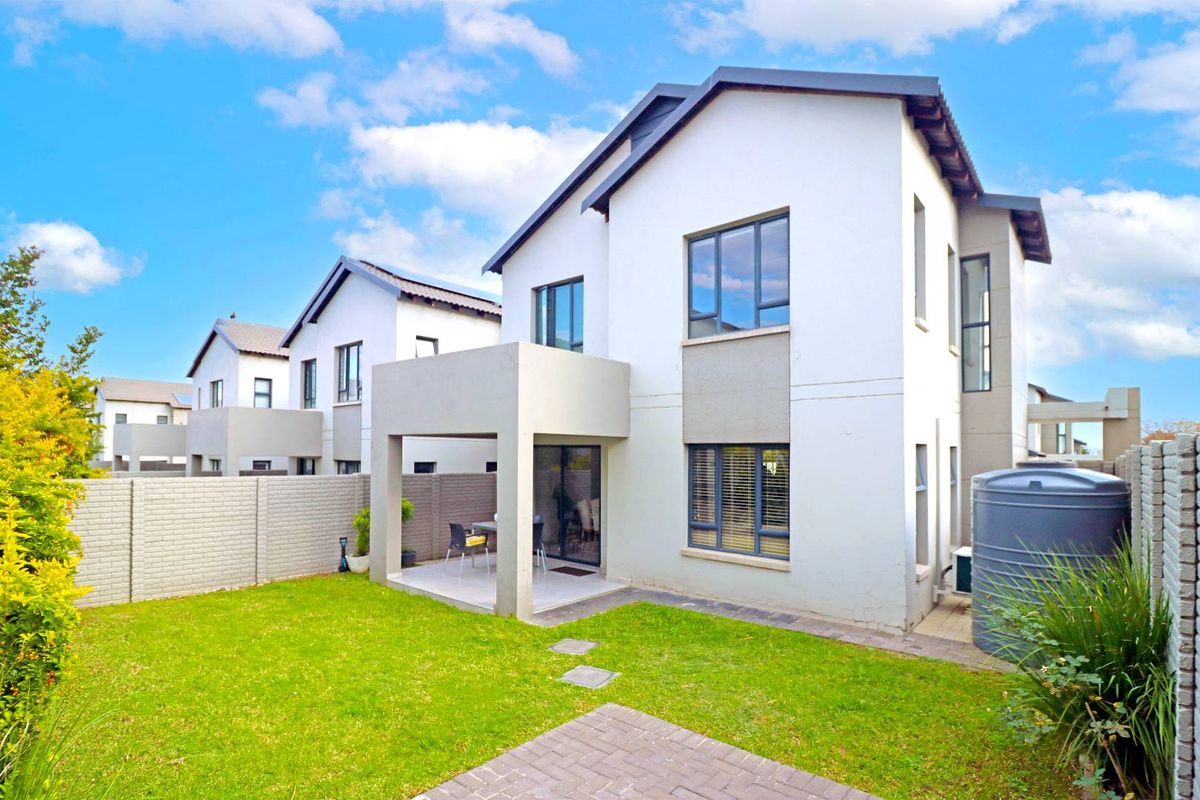 Rear view of a modern townhouse featuring a covered patio, private garden, and a water storage tank.
