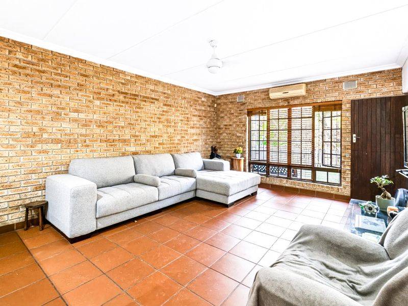 Spacious living room featuring exposed brick walls, ceramic tile flooring, and a split-system air conditioner, offering a comfortable and functional living space.
