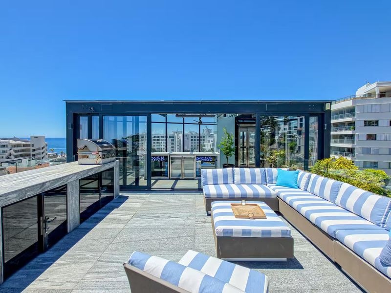Spacious penthouse terrace featuring stone flooring, a built-in barbecue station with stone countertops, and large glass sliding doors leading to the interior.
