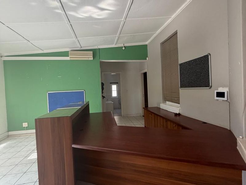 An office space featuring a built-in reception desk, tiled flooring, and a drop ceiling with integrated lighting.