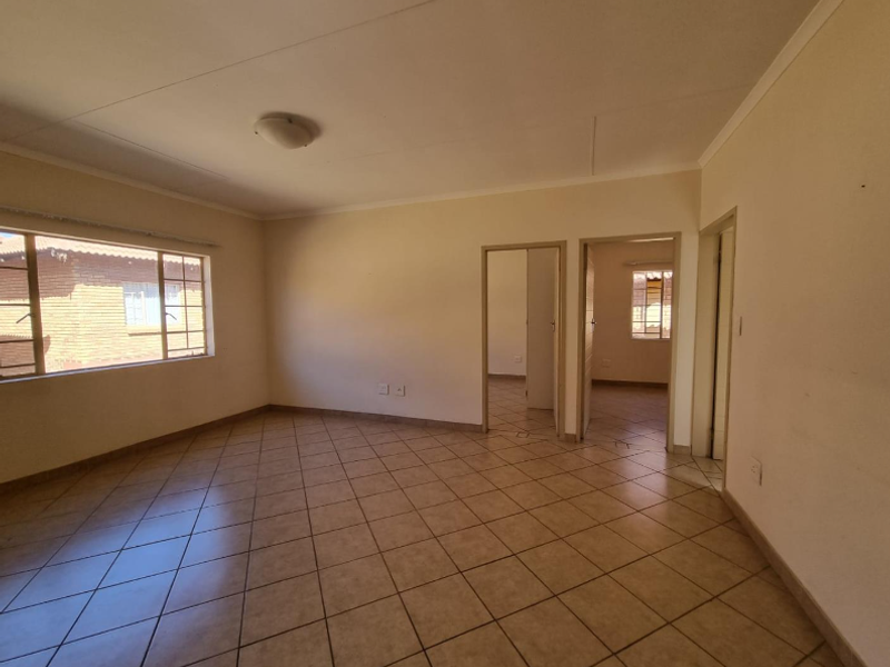 A spacious, empty living area featuring neutral ceramic floor tiles, clean walls, and multiple doorways leading to adjacent rooms.