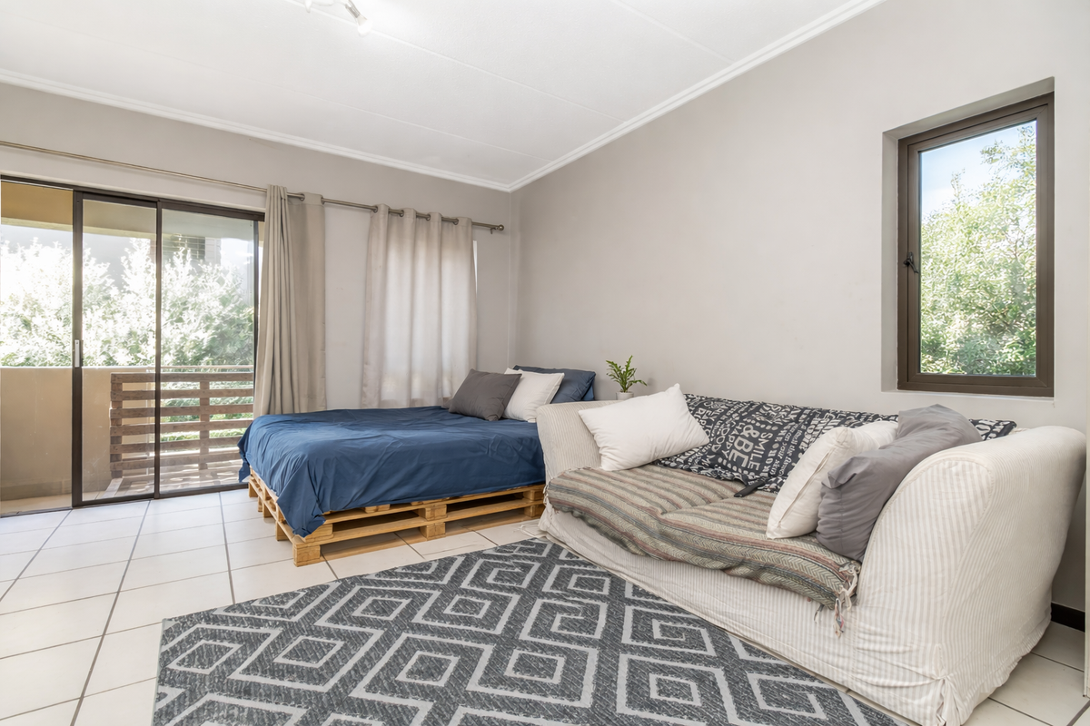 A bright bedroom featuring tiled flooring, large sliding glass doors leading to a private balcony, and a window providing natural light.