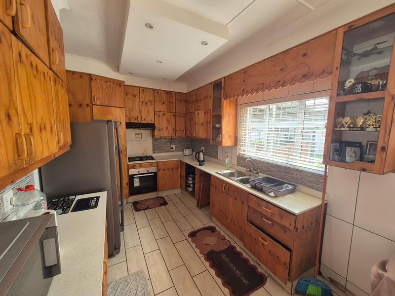 A functional kitchen featuring extensive wooden cabinetry, built-in oven, gas hob, and a double basin sink with tiled flooring and recessed lighting.