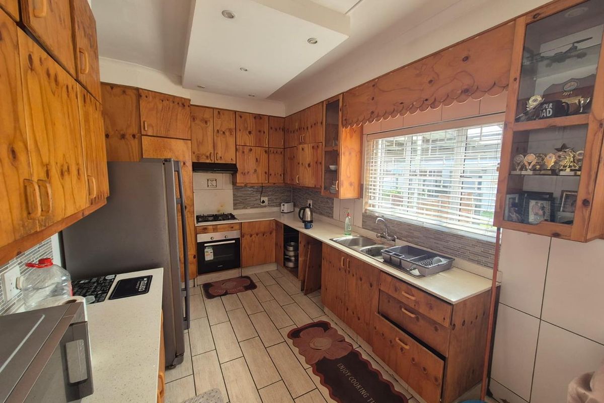 A functional kitchen featuring extensive wooden cabinetry, built-in oven, gas hob, and a double basin sink with tiled flooring and recessed lighting.