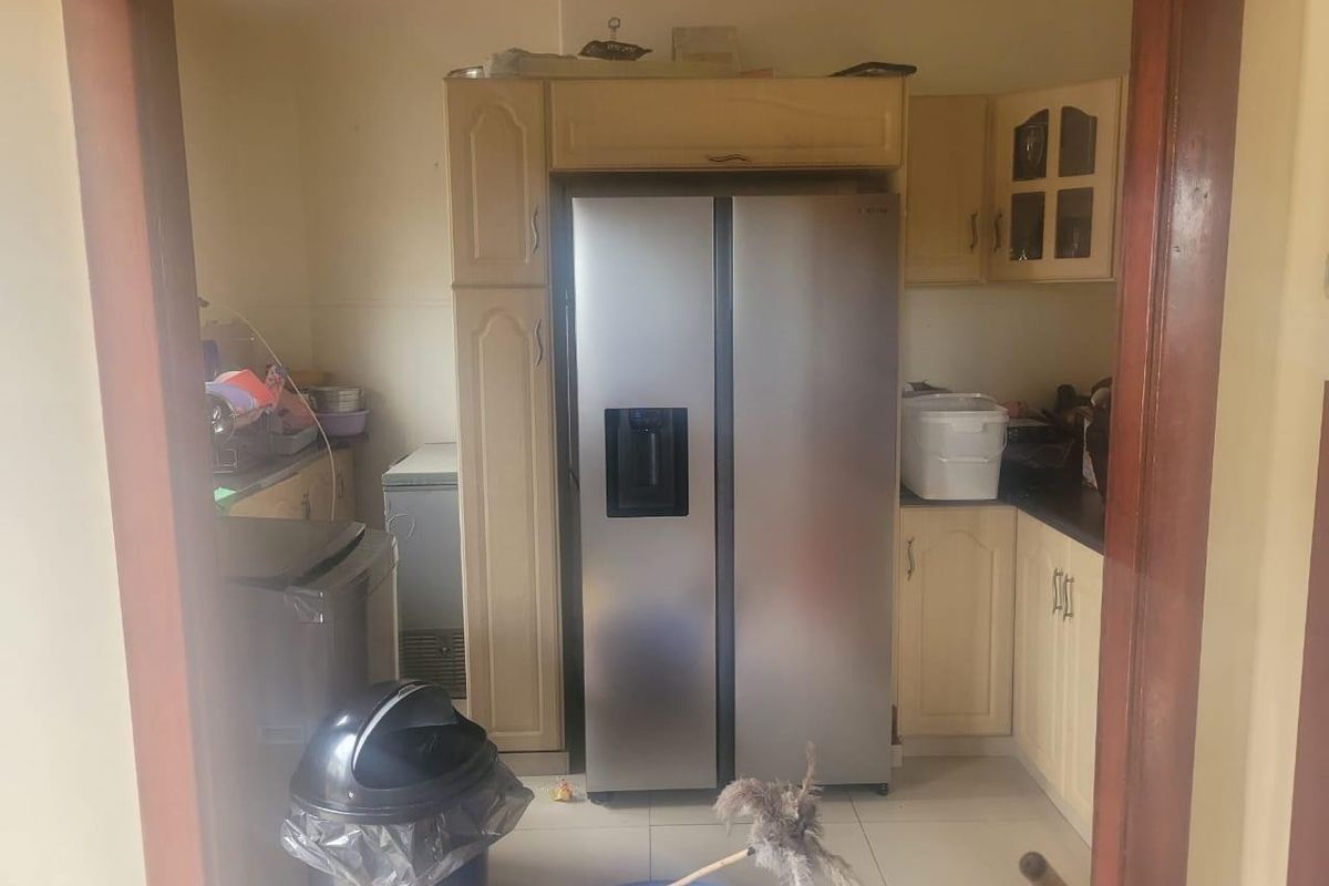 A dated kitchen area featuring built-in cabinetry and tiled flooring, currently used for storage and food preparation.