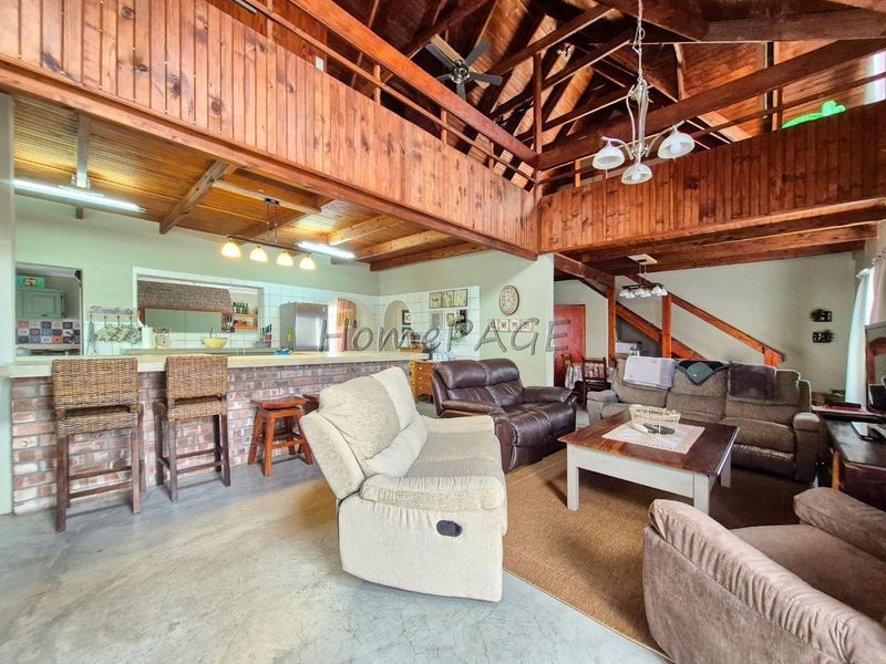 Spacious open-plan living area featuring exposed timber beams, a mezzanine level, brick breakfast bar, and concrete flooring with a rustic aesthetic.