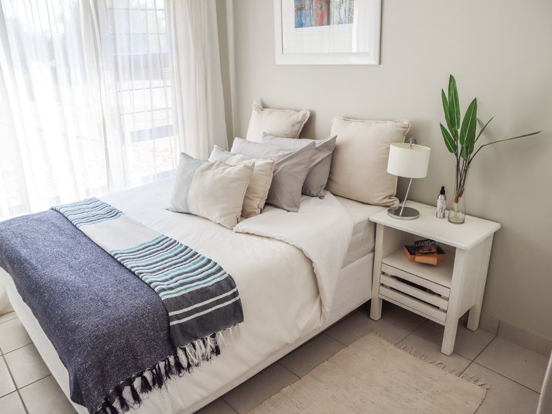 A bright and well-maintained bedroom featuring neutral wall tones, tiled flooring, and a large window allowing for ample natural light.
