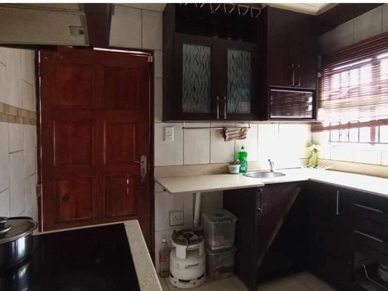 A functional kitchen featuring dark built-in cabinetry, laminate countertops, a stainless steel sink, and an electric hob with an overhead extractor fan.