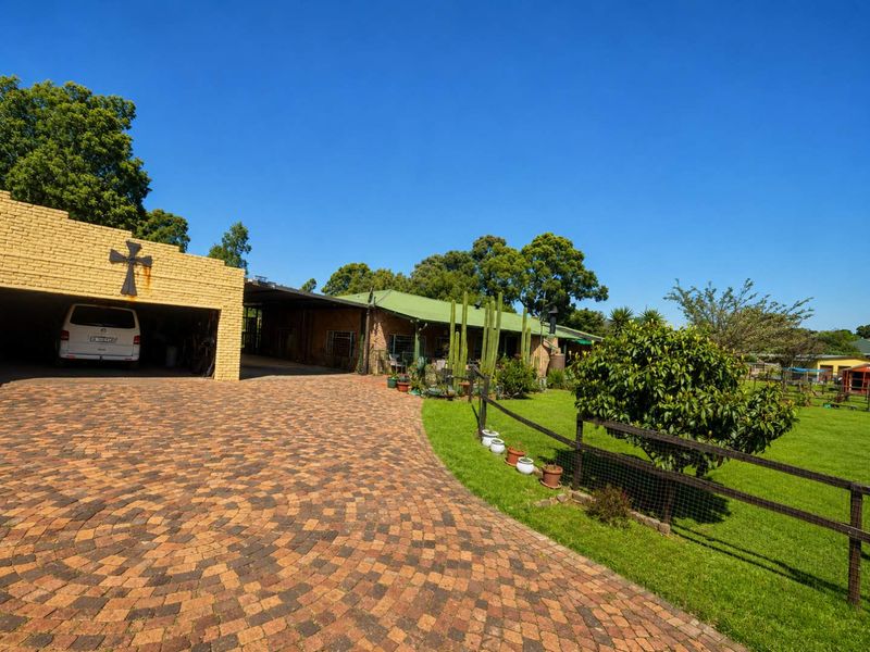 Front view of the small holding featuring a large brick paved driveway, covered carport, and well-maintained garden area with perimeter fencing.