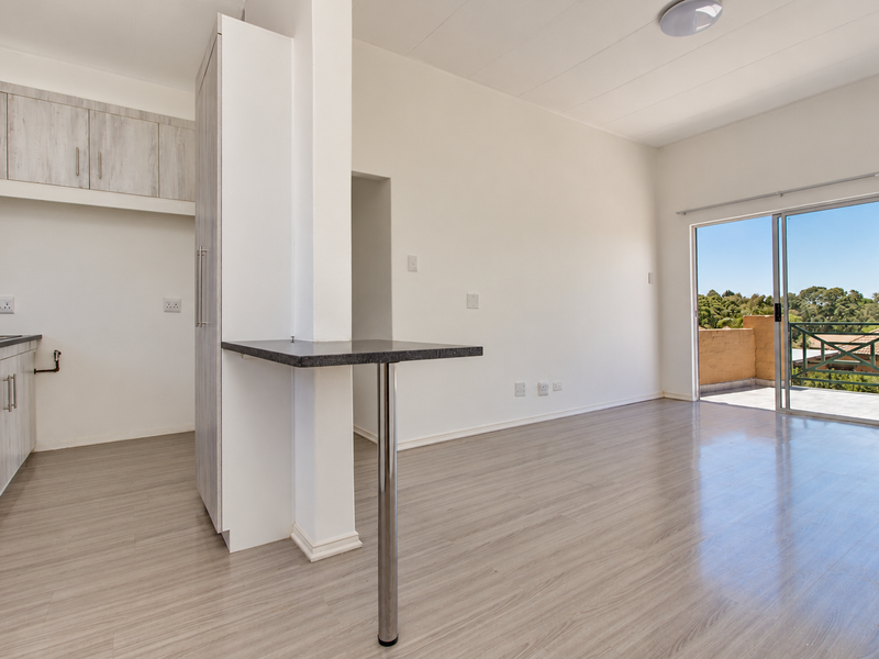 Bright open-plan living area featuring modern laminate flooring, a functional kitchen with built-in cabinetry, and a sliding door leading to a private balcony.