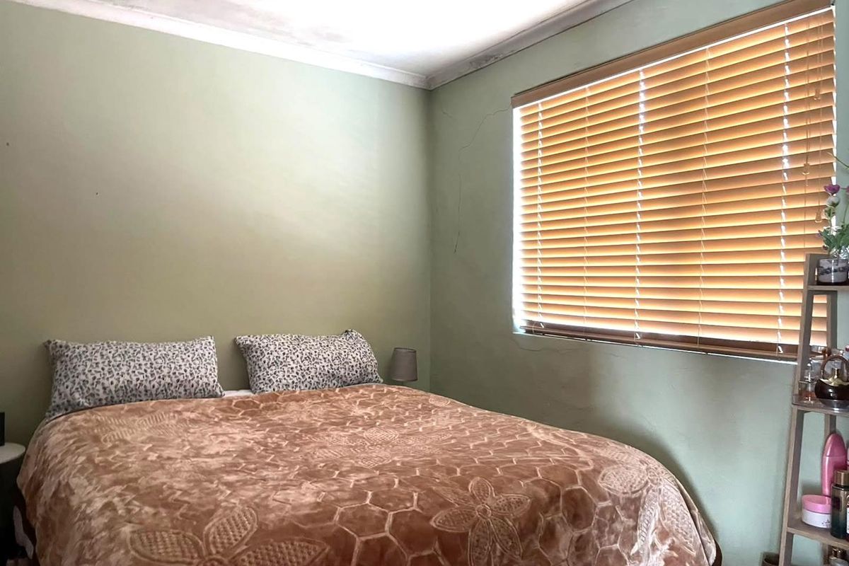 A bedroom featuring green walls, a window with fitted wooden blinds, and visible signs of wall cracking and ceiling water damage.