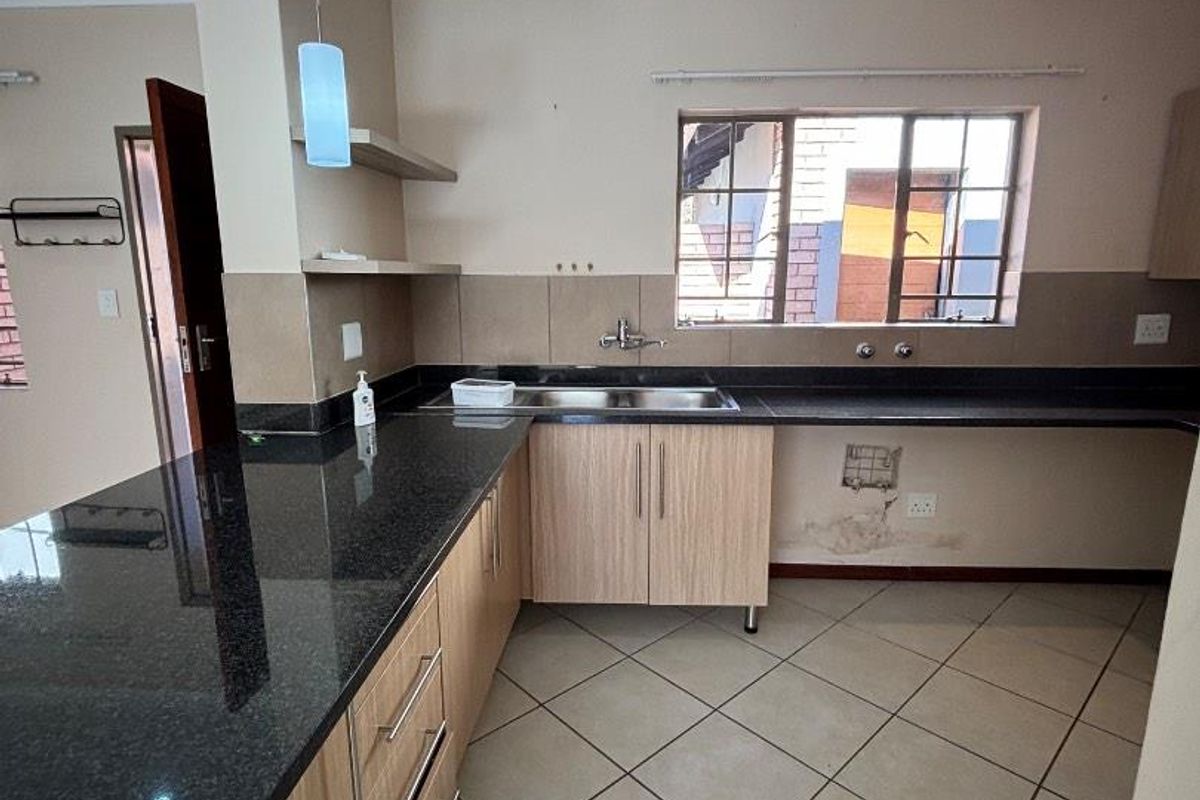 A kitchen featuring dark granite countertops, light wood cabinetry, tiled flooring, and a stainless steel sink, requiring some maintenance and cosmetic repairs.