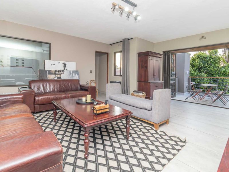 Spacious living room featuring large format floor tiles, modern track lighting, and seamless access to an outdoor balcony through sliding glass doors.
