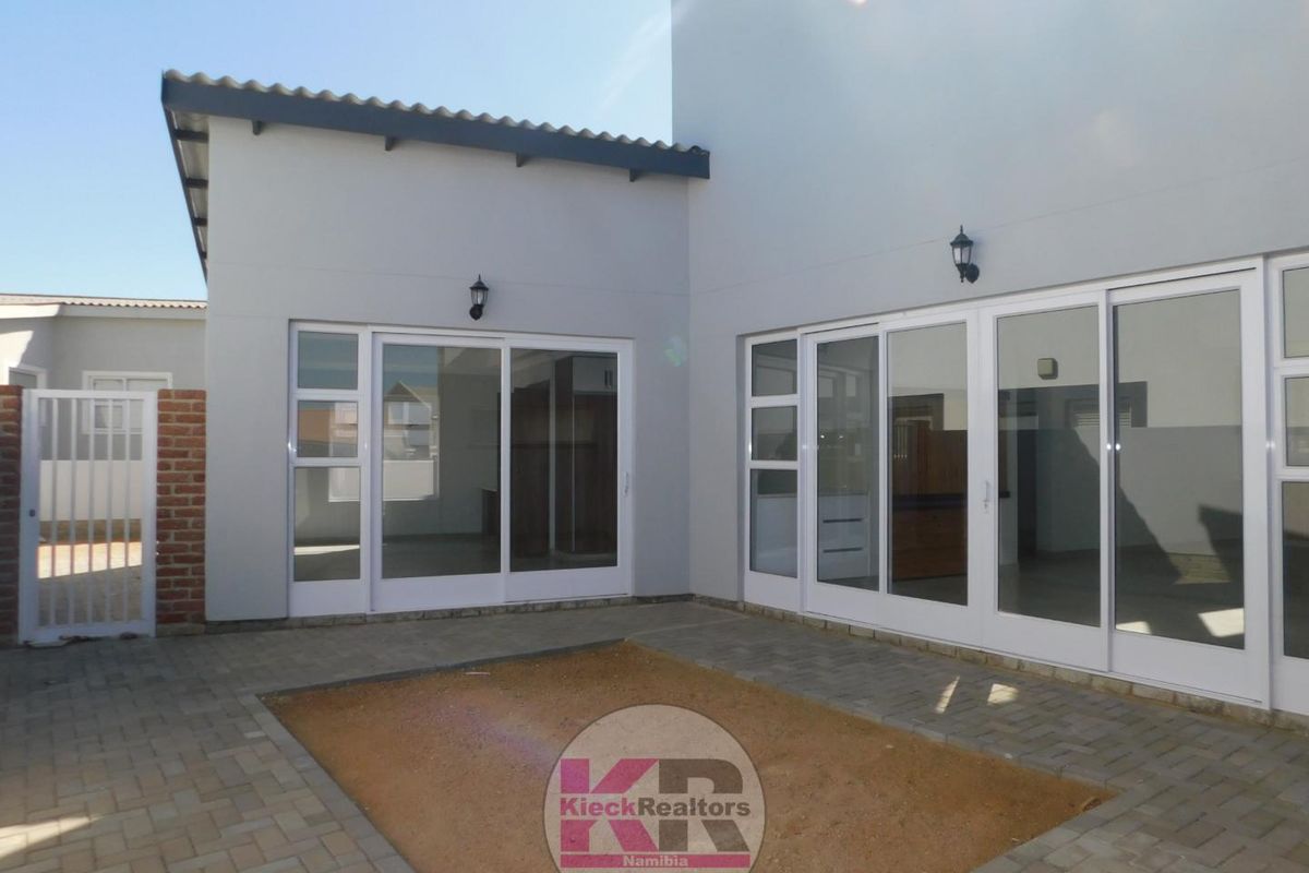 Rear exterior view of the property featuring paved courtyard area, sliding glass doors, and exterior wall-mounted lighting fixtures.