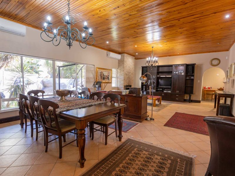 Spacious open-plan living and dining area featuring a warm timber ceiling, stone-clad fireplace, built-in cabinetry, and large sliding doors leading to the garden.