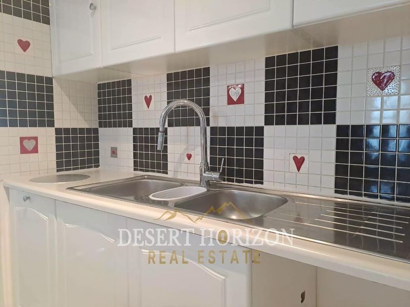 A kitchen sink area featuring white shaker-style cabinetry and a distinctive black and white checkerboard mosaic tile backsplash with decorative accents.