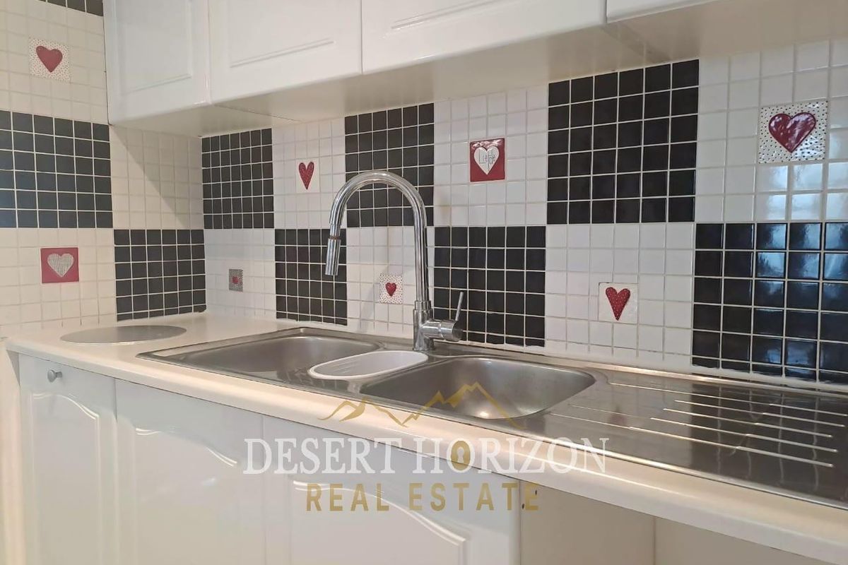 A kitchen sink area featuring white shaker-style cabinetry and a distinctive black and white checkerboard mosaic tile backsplash with decorative accents.