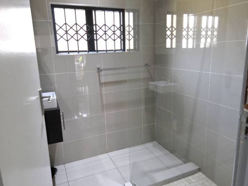 Modern bathroom featuring a walk-in shower with glass screen, wall-mounted vanity, and neutral floor-to-ceiling tiling.