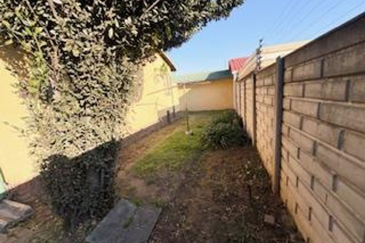 A narrow rear garden area featuring a precast concrete boundary wall with electric fencing and a small paved section.