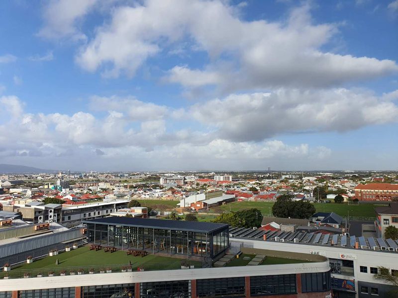 Elevated panoramic view overlooking the surrounding urban landscape, featuring a rooftop terrace with a modern glass-enclosed structure and artificial lawn.