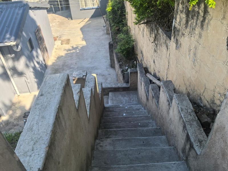 An outdoor concrete staircase leading down to a paved rear yard area, featuring a weathered retaining wall with visible surface cracking.