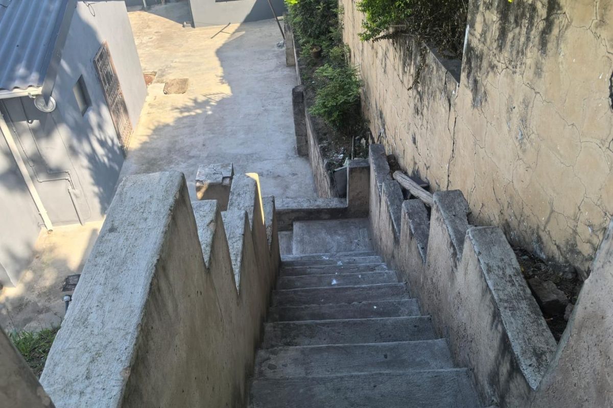 An outdoor concrete staircase leading down to a paved rear yard area, featuring a weathered retaining wall with visible surface cracking.