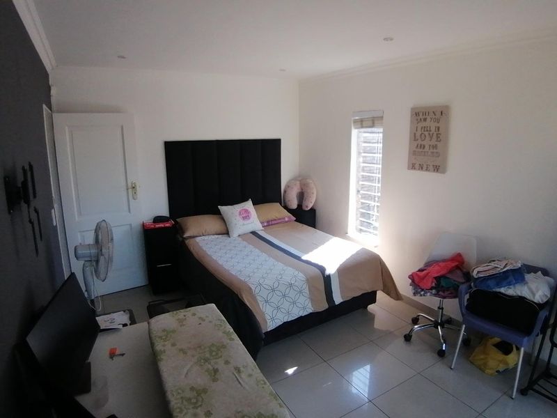 A well-lit bedroom featuring neutral tiled flooring, recessed ceiling lighting, and a vertical window blind, offering a functional and comfortable living space.