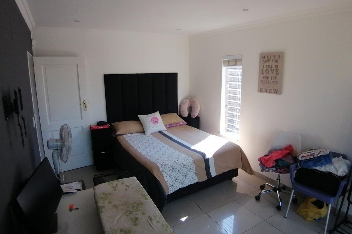 A well-lit bedroom featuring neutral tiled flooring, recessed ceiling lighting, and a vertical window blind, offering a functional and comfortable living space.