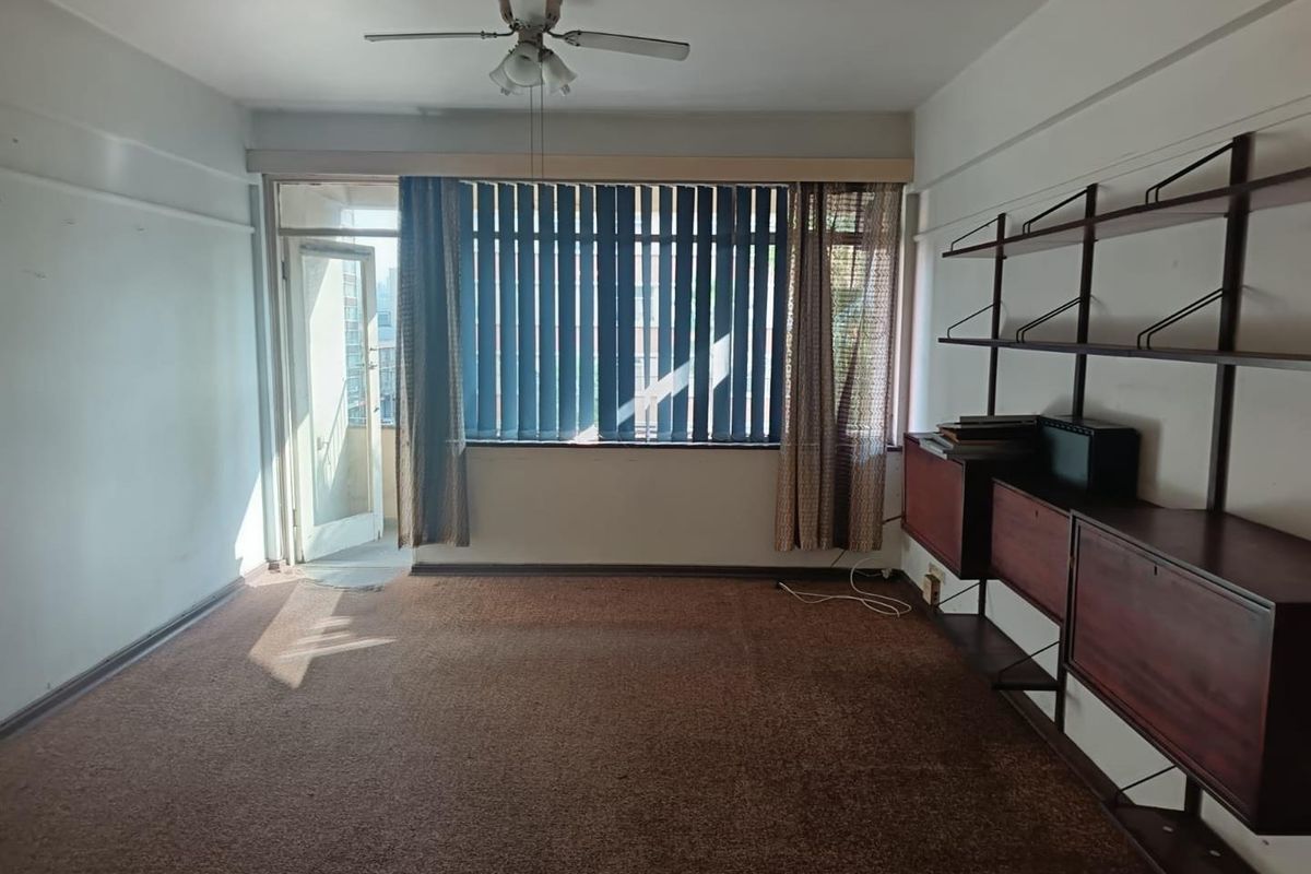 Spacious living room featuring a ceiling fan, wall-mounted shelving, and direct access to a balcony through a glass door.