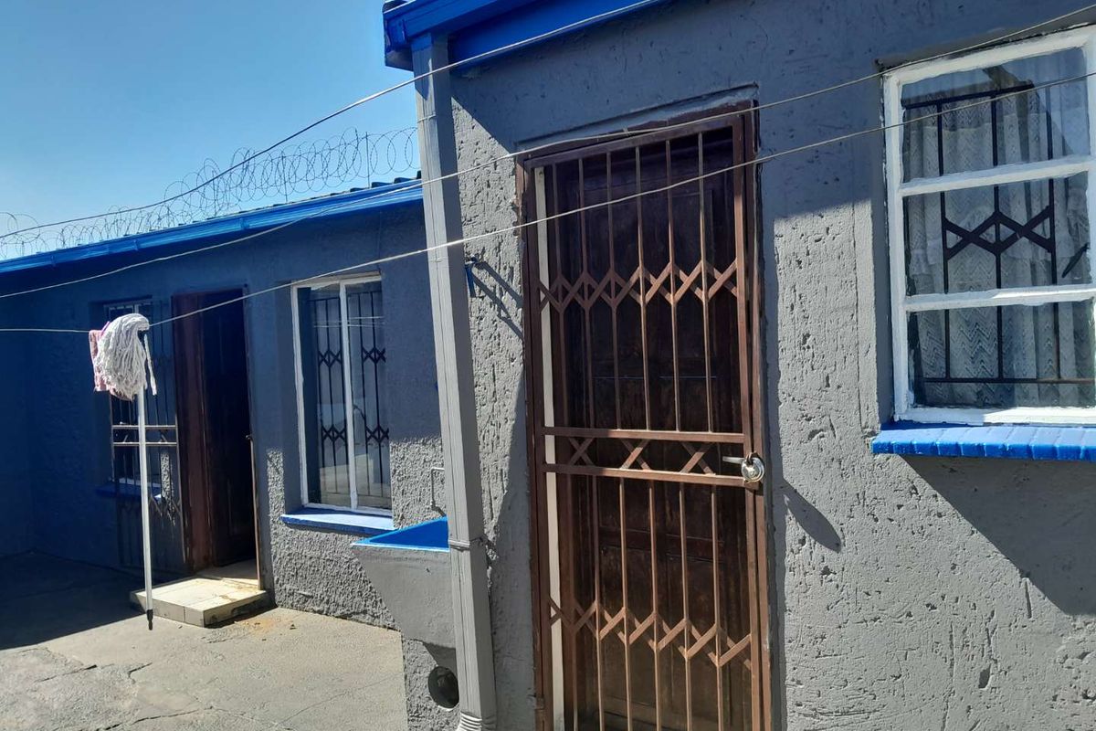 Rear exterior view of the property featuring textured walls, security gates, window bars, and an external wash basin.
