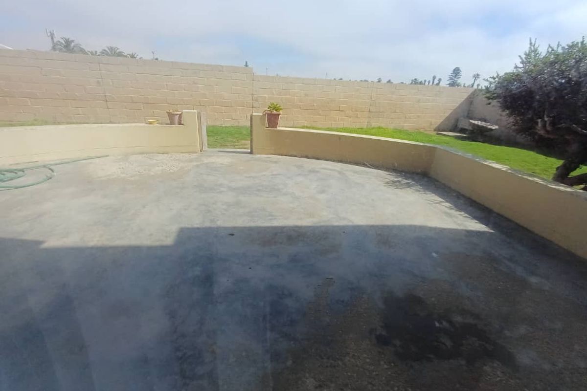 A spacious rear outdoor area featuring a concrete patio, low retaining walls, and a perimeter boundary wall.